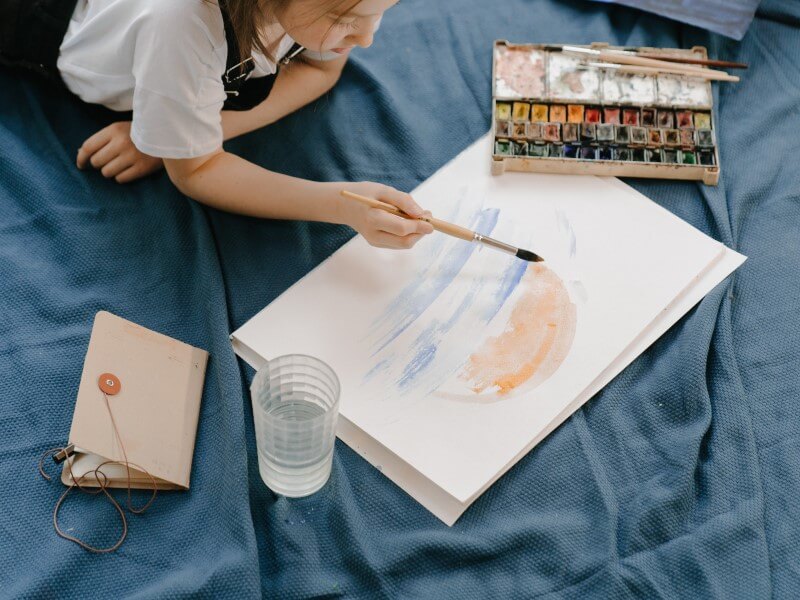girl holding paintbrush and painting on white paper indoor activities for kids