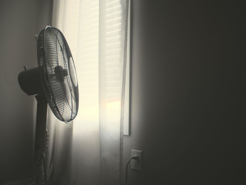 a standing fan in front of a window