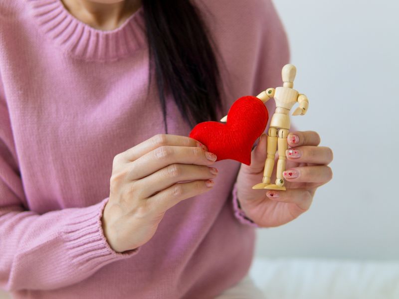 A person holding love-shaped object and a human-shaped wooden caricature 