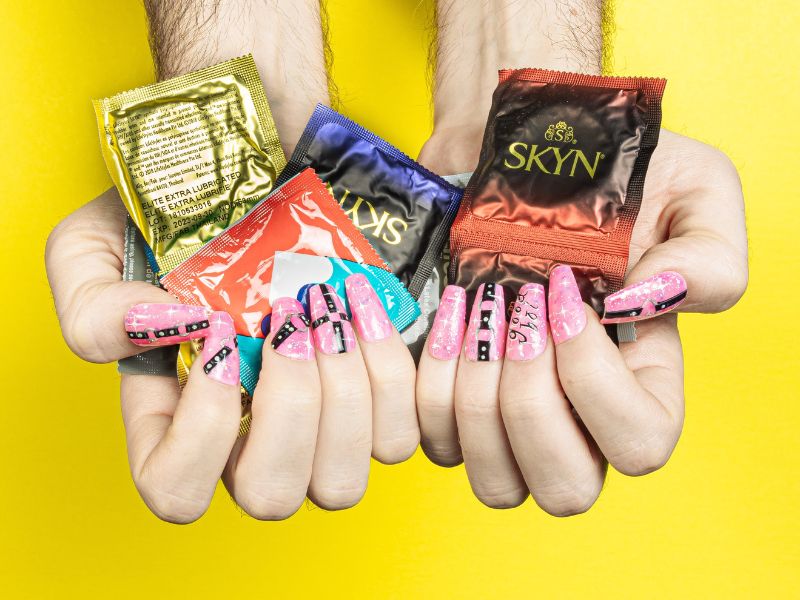 A pair of hands holding various condom packets
