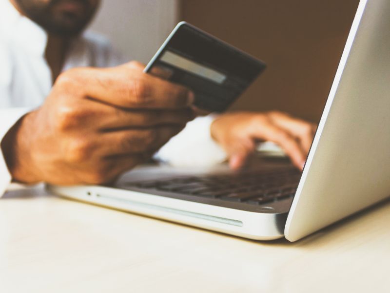 a person holding a credit card while working on a laptop online scams in malaysia