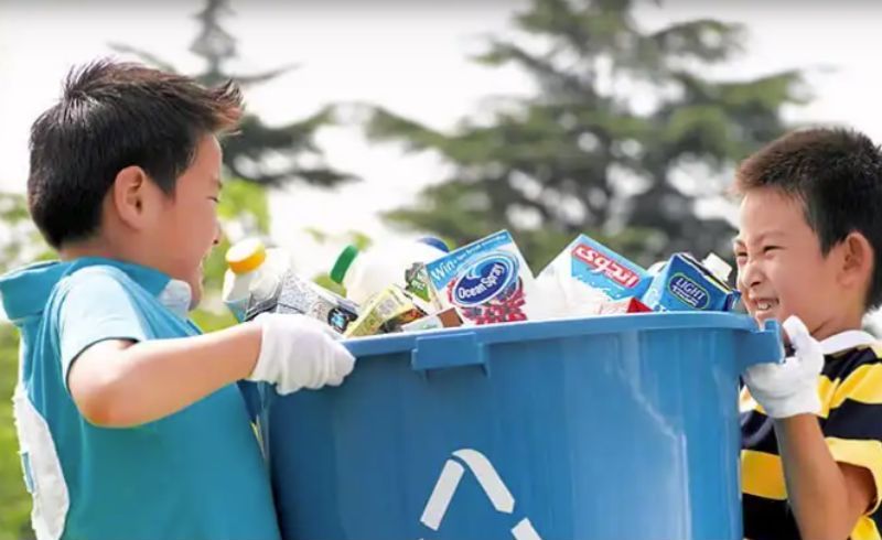 two kids carrying a recycling bin