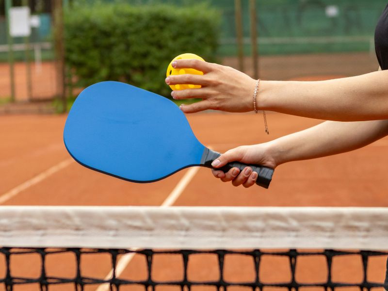 hands holding a pickleball racquet and ball